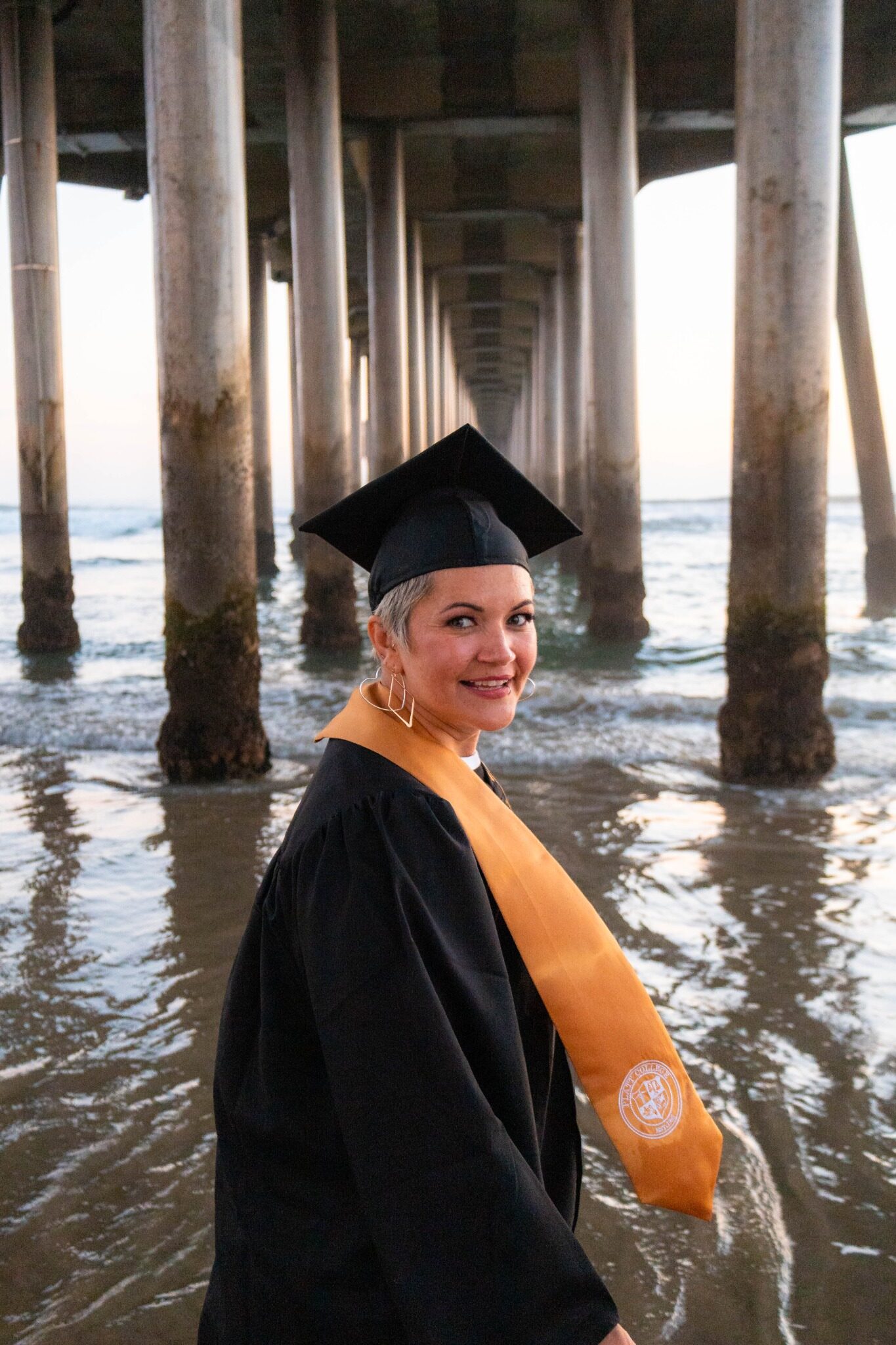 Graduate celebrating beneath a beach pier