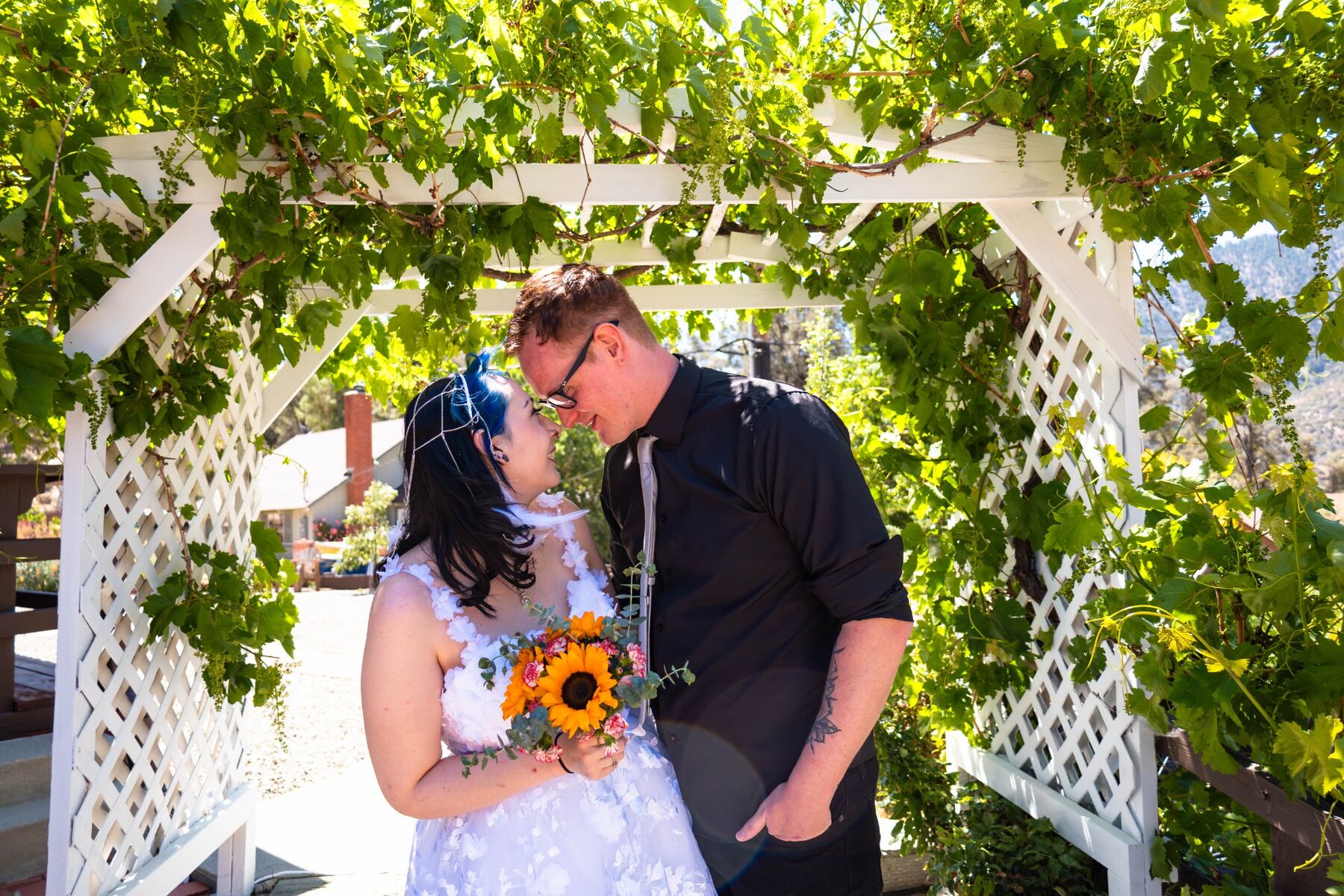 Newlyweds touching foreheads beneath a leafy garden arbor